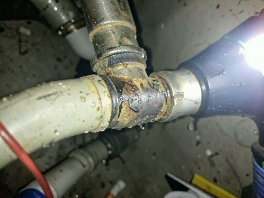 A corroded, leaking pipe joint under a sink